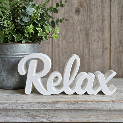 White Relax sign on wooden surface with potted plant – minimalist bathroom decor, made in USA